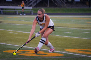 Field hockey player in motion, skillfully maneuvering to control the ball on a green turf field during a game.