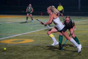 A field hockey match at night with players competing for the ball on a vibrant turf field.