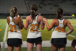 Three young athletes in jerseys hold hands, ready for a game under stadium lights, showcasing teamwork and camaraderie.