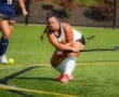 Field hockey player in action, focused on hitting the ball during a match on a bright green turf field.