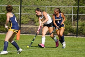 Field hockey players compete for the ball during an intense match on a sunny day at the sports field.