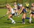 High school field hockey players competing on a sunny day, focusing on teamwork and skill on the turf field.