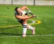A field hockey player strikes the ball on a turf field, showcasing athleticism and skill during a game.