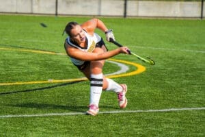 A field hockey player strikes the ball on a turf field, showcasing athleticism and skill during a game.