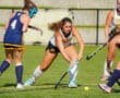 Female field hockey players in action during a competitive match on a sunny day, showcasing teamwork and skill.