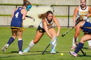Female field hockey players in action during a competitive match on a sunny day, showcasing teamwork and skill.