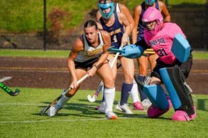 Field hockey match in action, showcasing players in motion, including a goalie in pink and a focused attacker.
