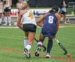 Two female field hockey players compete for the ball on a green turf field during a match.