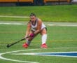 Field hockey player in action, dribbling a ball on turf during a game, showcasing athleticism and focus.
