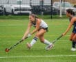 Two players compete for the ball during a lively field hockey match on a rainy day, showcasing athleticism and teamwork.