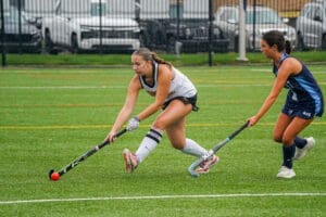 Two players compete for the ball during a lively field hockey match on a rainy day, showcasing athleticism and teamwork.
