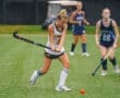 High school field hockey players compete in a rain-soaked match, showcasing skill and teamwork on the turf.