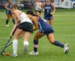 Two field hockey players compete for the ball on a rainy day, showcasing athleticism and teamwork during a game.