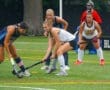 High school field hockey players competing for the ball on a rain-soaked turf field during a match.