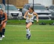 High school field hockey players competing on a rainy turf, showcasing athletic skill and teamwork during the match.