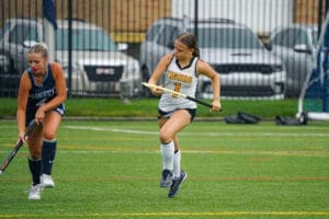 High school field hockey players competing on a rainy turf, showcasing athletic skill and teamwork during the match.