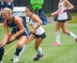 Two young athletes compete in a field hockey match, showcasing skill and determination on a rainy day.