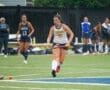 High school field hockey player in action during a rainy game, showcasing skills on the turf with teammates in the background.