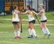 Field hockey players celebrate a goal, showing teamwork and excitement on a rainy day.