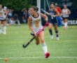 Field hockey player in action, dribbling the ball on a turf field during a competitive match.