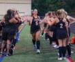 Field hockey team celebrates a player with high-fives before a game, showcasing teamwork and sports spirit.