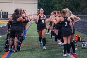 Field hockey team celebrates a player with high-fives before a game, showcasing teamwork and sports spirit.
