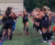 Field hockey team celebrates a player running through a tunnel of teammates in a lively game atmosphere.