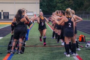 Field hockey team celebrates a player running through a tunnel of teammates in a lively game atmosphere.