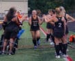 Team celebrating as a player runs through a tunnel of teammates in a high school field hockey match.