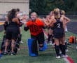 High school field hockey team celebrates a goalie in orange uniform running through a cheering line of teammates.