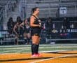 Field hockey player in action during a rainy match, showcasing determination on the field with teammates in the background.