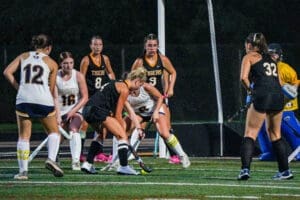 High school field hockey match in progress, players in action with lights illuminating the field at night.