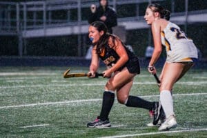 Field hockey players compete in the rain, showcasing athleticism and determination on the turf.