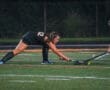 Field hockey players compete for the ball on a turf field during a night game, showcasing skill and athleticism.