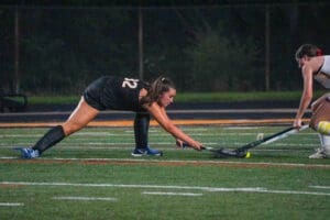 Field hockey players compete for the ball on a turf field during a night game, showcasing skill and athleticism.