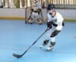 Young hockey player skillfully maneuvers on a blue rink, wearing a white jersey and black protective gear.