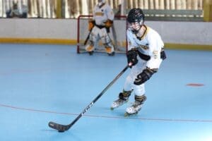 Young hockey player skillfully maneuvers on a blue rink, wearing a white jersey and black protective gear.