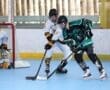 Two players compete for the puck in roller hockey, with one player in white and the other in green.