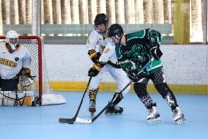 Two players compete for the puck in roller hockey, with one player in white and the other in green.