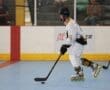 Young hockey player in a white uniform skating on a roller rink, focused on puck control and gameplay.