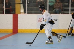 Young hockey player in a white uniform skating on a roller rink, focused on puck control and gameplay.
