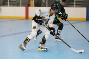 Two players compete in a roller hockey match, showcasing speed and agility on a blue rink surface.