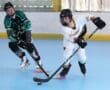 Two young players compete in a roller hockey match, showcasing skill and teamwork on a blue rink.