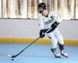 A roller hockey player in a white Tigers jersey skates with a stick, preparing to shoot a puck in a rink.