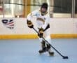 Young hockey player in roller skates, focused on maneuvering the puck in a rink, wearing a team jersey with Tigers.