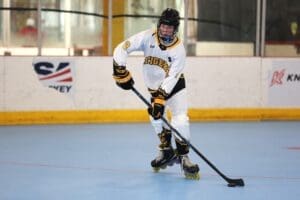 Young hockey player in roller skates, focused on maneuvering the puck in a rink, wearing a team jersey with Tigers.