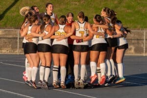 Field hockey team celebrating in a huddle, showcasing teamwork and unity on the field.