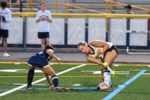 High school field hockey players compete for the ball on a turf field during an intense game.