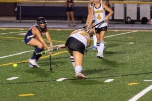Field hockey players in action on a turf field, showcasing teamwork and athleticism during a competitive match.