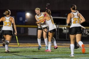 Cheering field hockey players celebrate a goal under the stadium lights, showcasing teamwork and excitement.